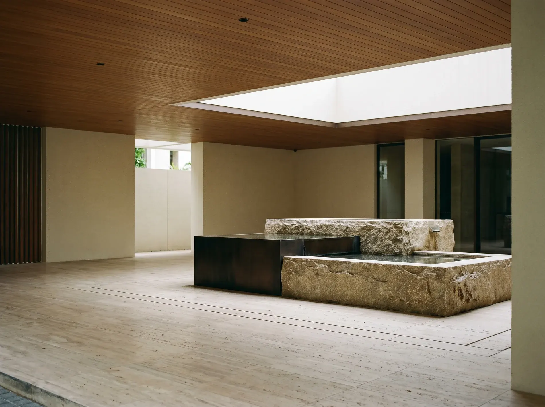 A hushed arrival court in a prime residence, stone water feature under a timber ceiling. A representative scene.