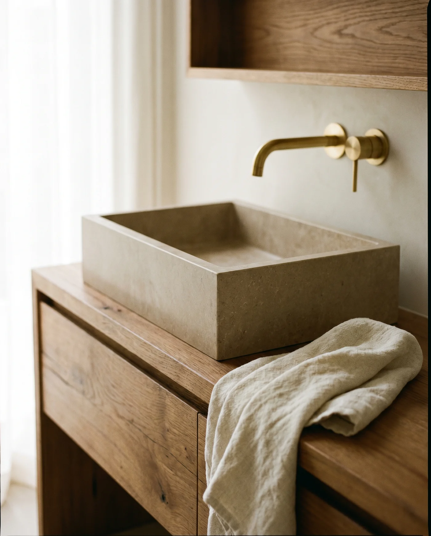 A stone basin on an oak vanity, wall-mounted brass tap, soft curtain light. A representative interior.