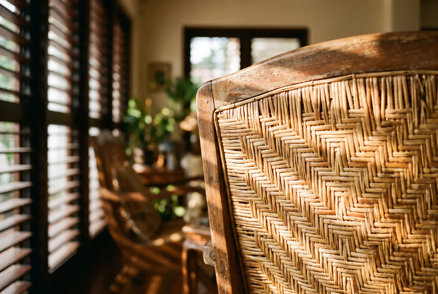 The woven rattan back of an old teak armchair in golden light from louvred windows.
