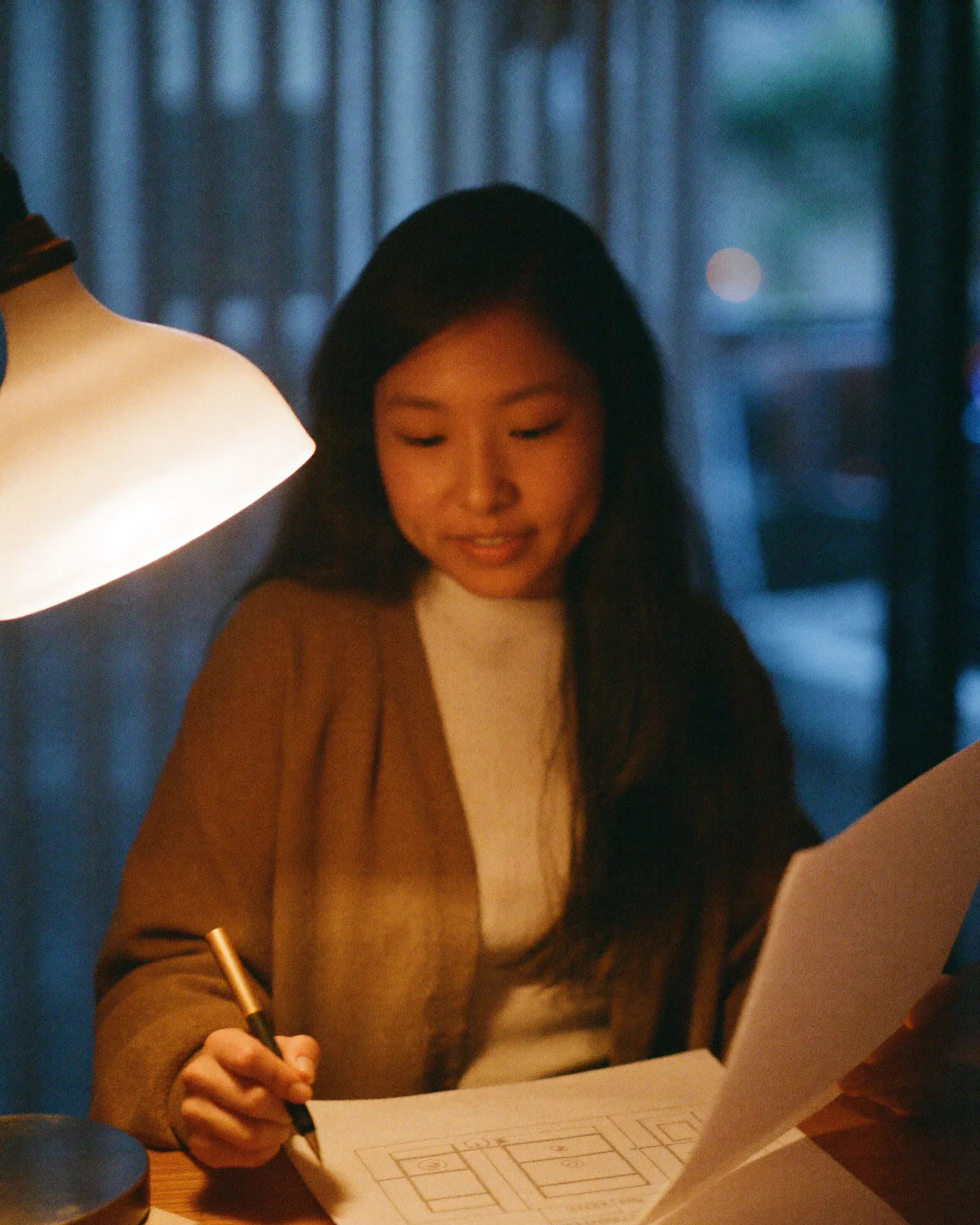 Jessin reading plans at a lamp-lit desk in the evening. A representative scene.