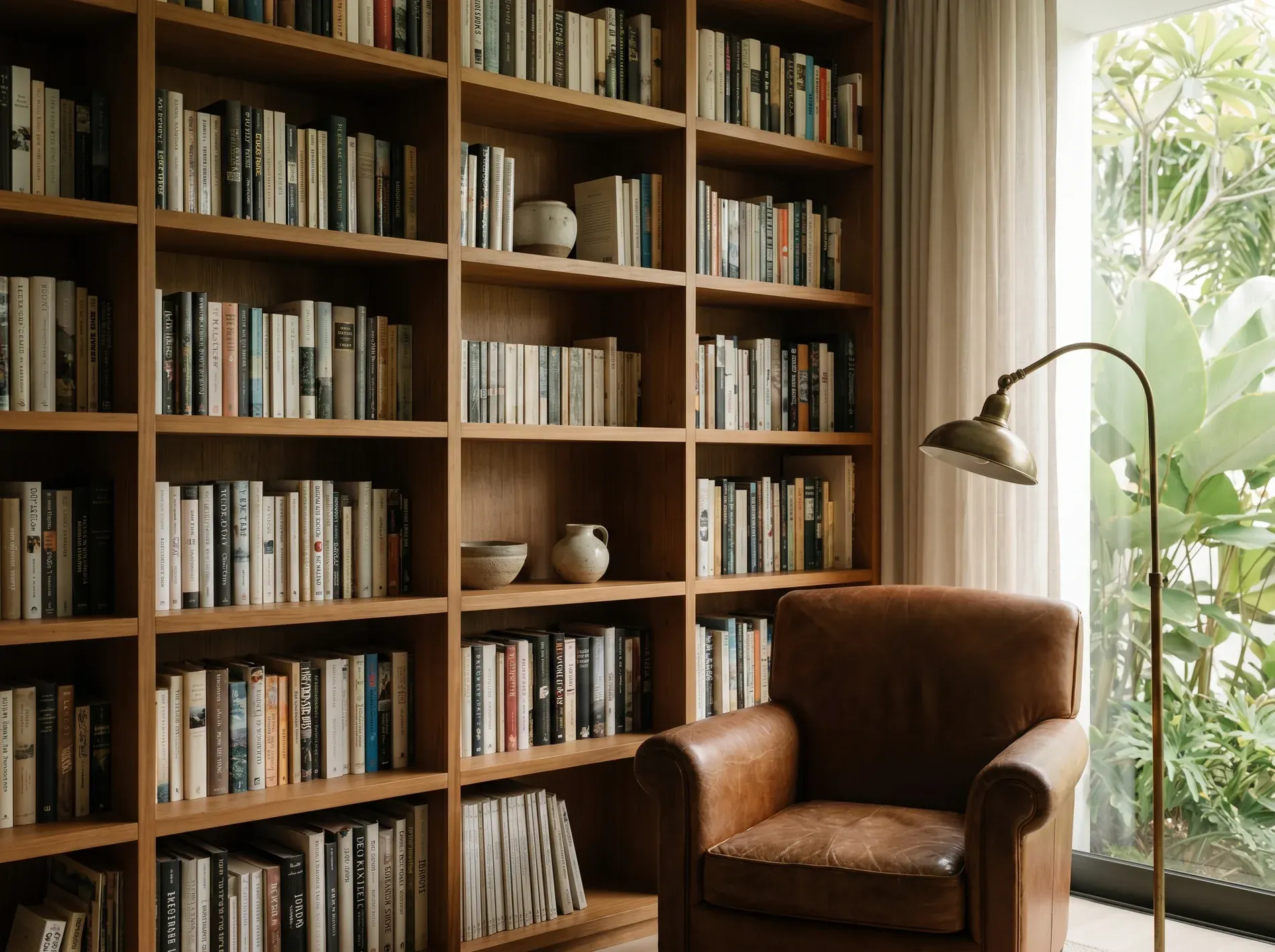 A timber study wall of books with a worn leather armchair and brass reading lamp by the garden window. A representative scene.
